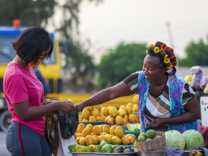 An African American female in a protective face mask shopping for fruit at a market