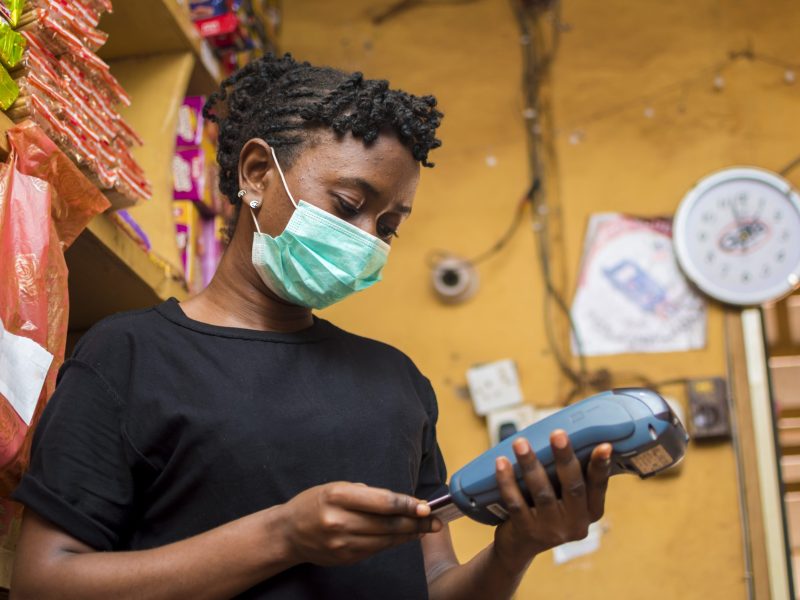 young african female attendant using the point of sale machine to pay for the goods her customer bought while using face mask to prevent herself from the corona outbreak.
